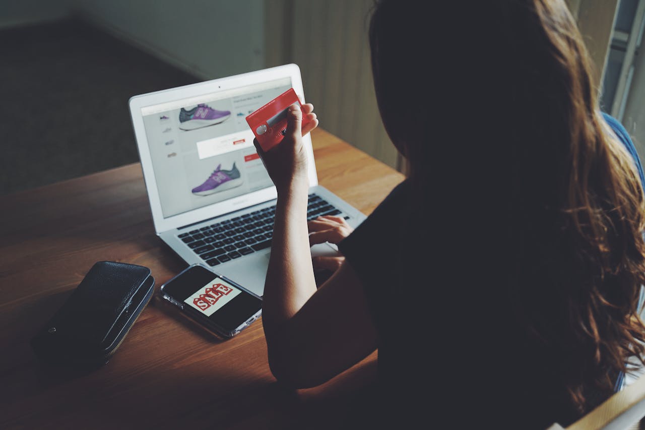 A woman shops online using a laptop and credit card on a wooden table.